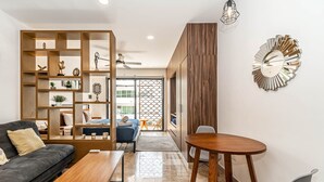 A modern living room with a sofa, coffee table, and a dining area with a table and chairs. There is a decorative wall piece and a ceiling fan. - Ocean View Apt 2 blocks away from beach (Playa del Carmen)