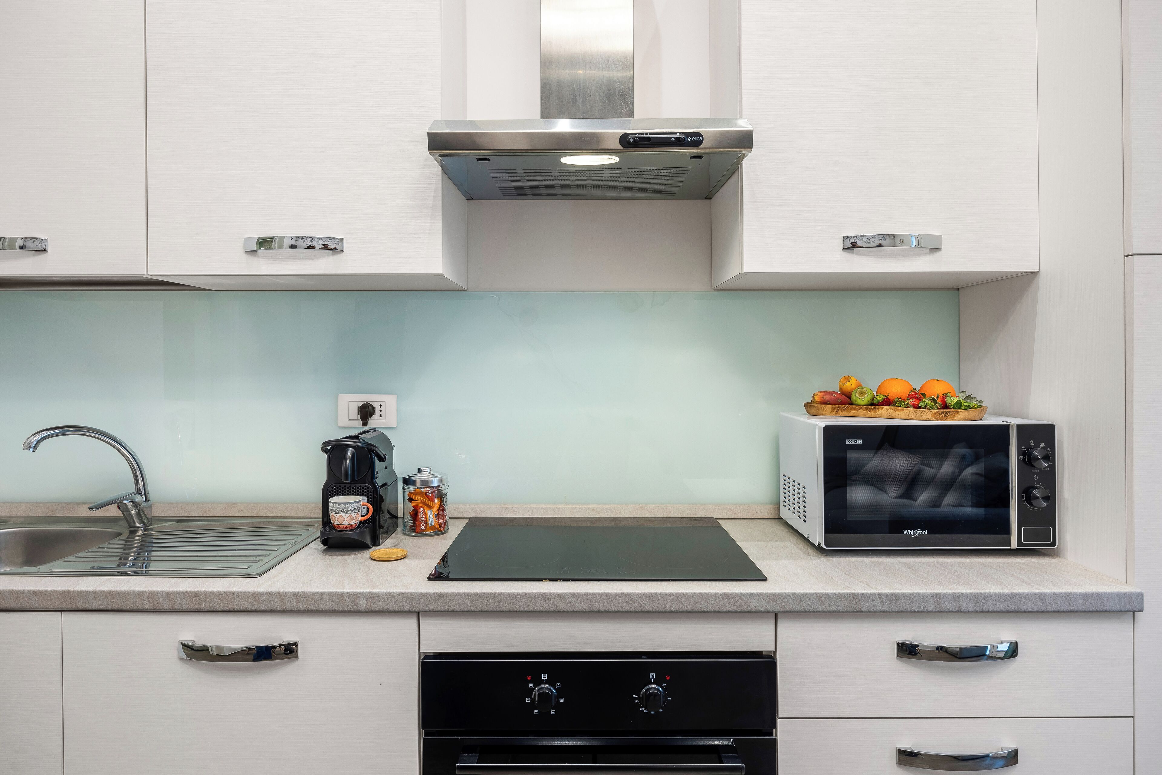Una cucina moderna con cappa in acciaio inossidabile, microonde, lavello e lavastoviglie.