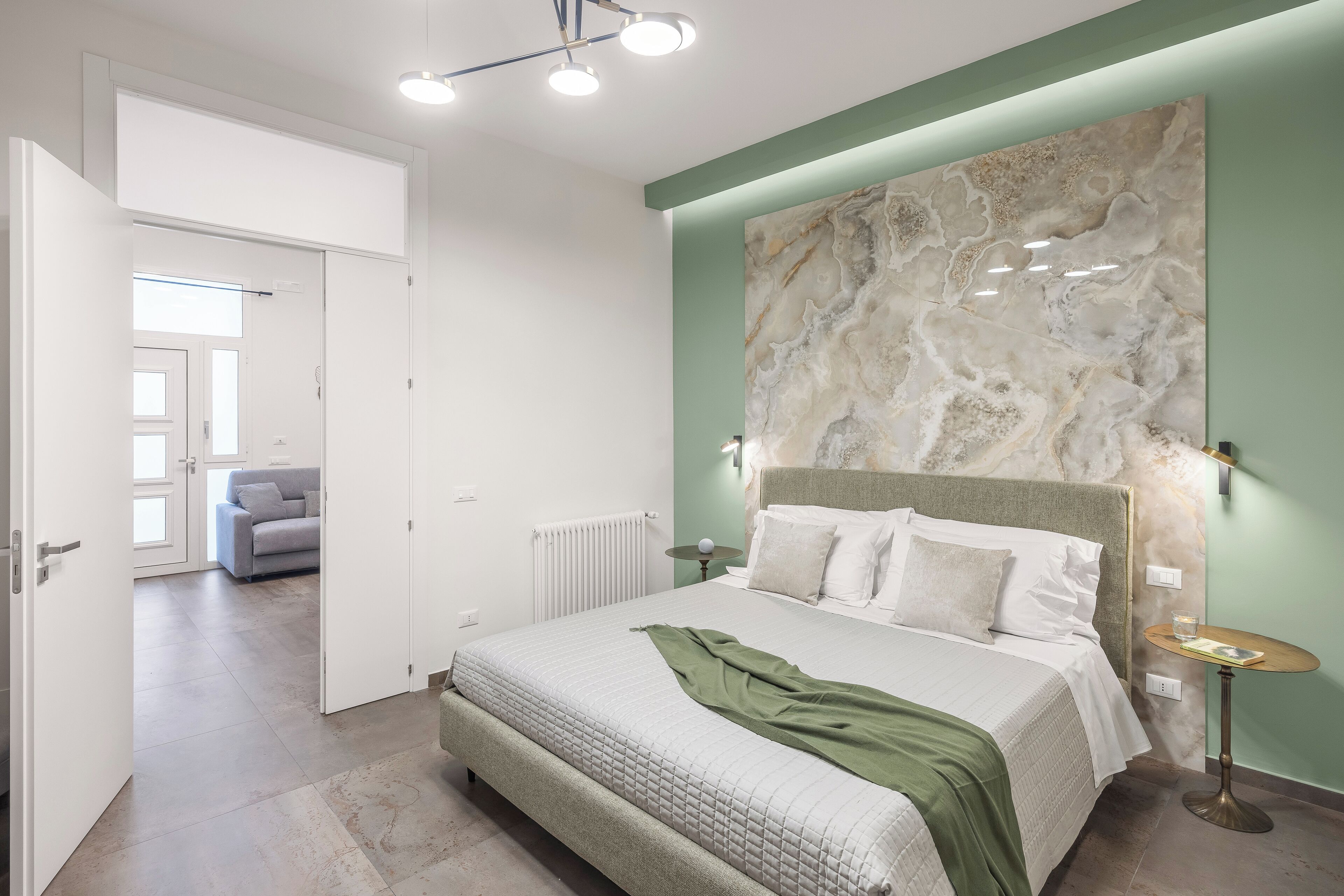 A modern bedroom with a large bed, a marble accent wall, and a view into another room.