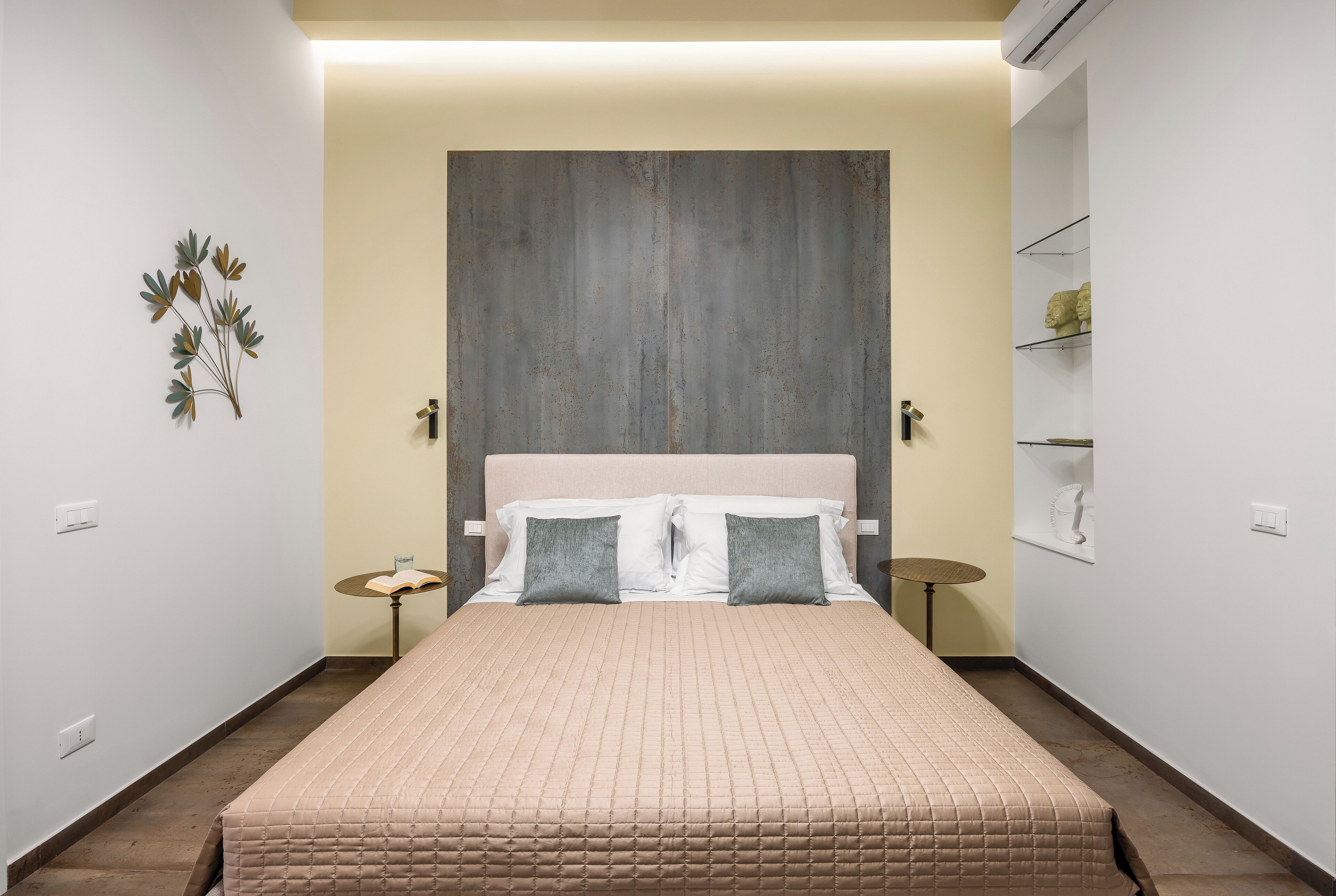 Une chambre à coucher avec un grand lit, une tête de lit, des tables de chevet et une étagère fixée au mur.