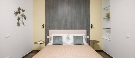 Une chambre à coucher avec un grand lit, une tête de lit, des tables de chevet et une étagère fixée au mur.