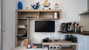 A compact living space with a TV mounted on a wall, a wooden desk with a coffee machine, and a bookshelf filled with books. - Apartment in Agde near Beach & Heated Pool (Agde)