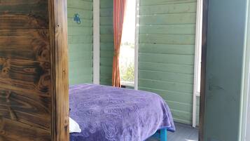Quarto com cama, paredes de madeira, janela com cortinas e teto com luminárias pendentes.