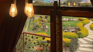 Een kamer met een schuine balkenplafond en uitzicht op een aangelegde tuin en verre bergen door grote ramen.