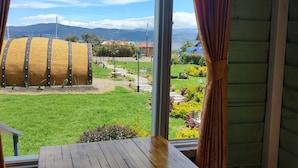 Een houten tafel en bankje in een kamer met uitzicht op een tuin en bergen door een raam.