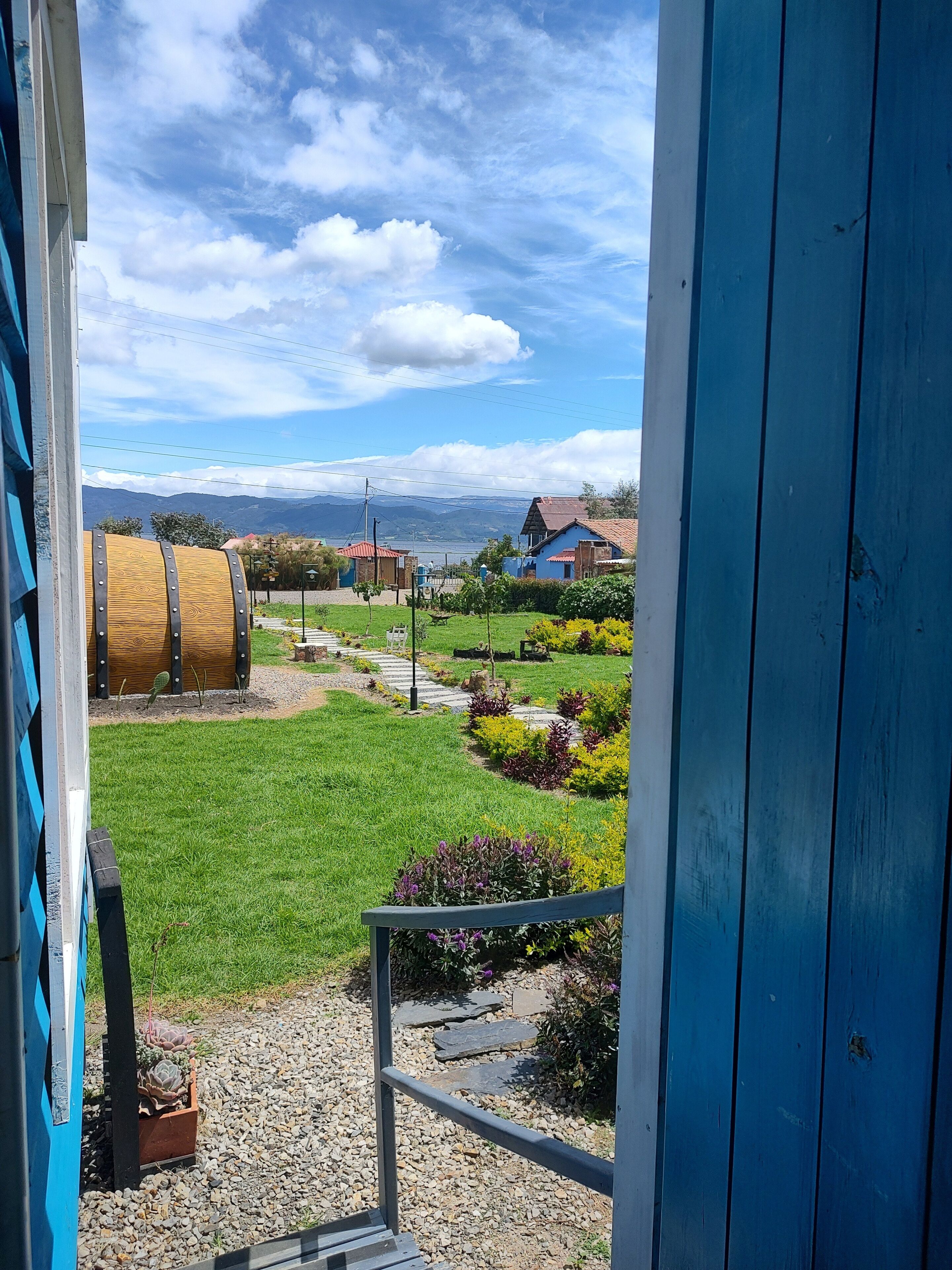 A view from a balcony overlooking a garden with a wooden barrel, a stone pathway, and a house with a red roof.