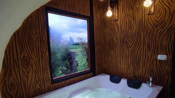 Een badkamer met een groot bad, een raam met uitzicht op groen en houten wandpanelen.