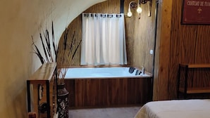 Een gezellige kamer met houten inrichting, een bed, een tafel met een fles wijn en een glas, en een uitzicht op een raam met gordijnen.