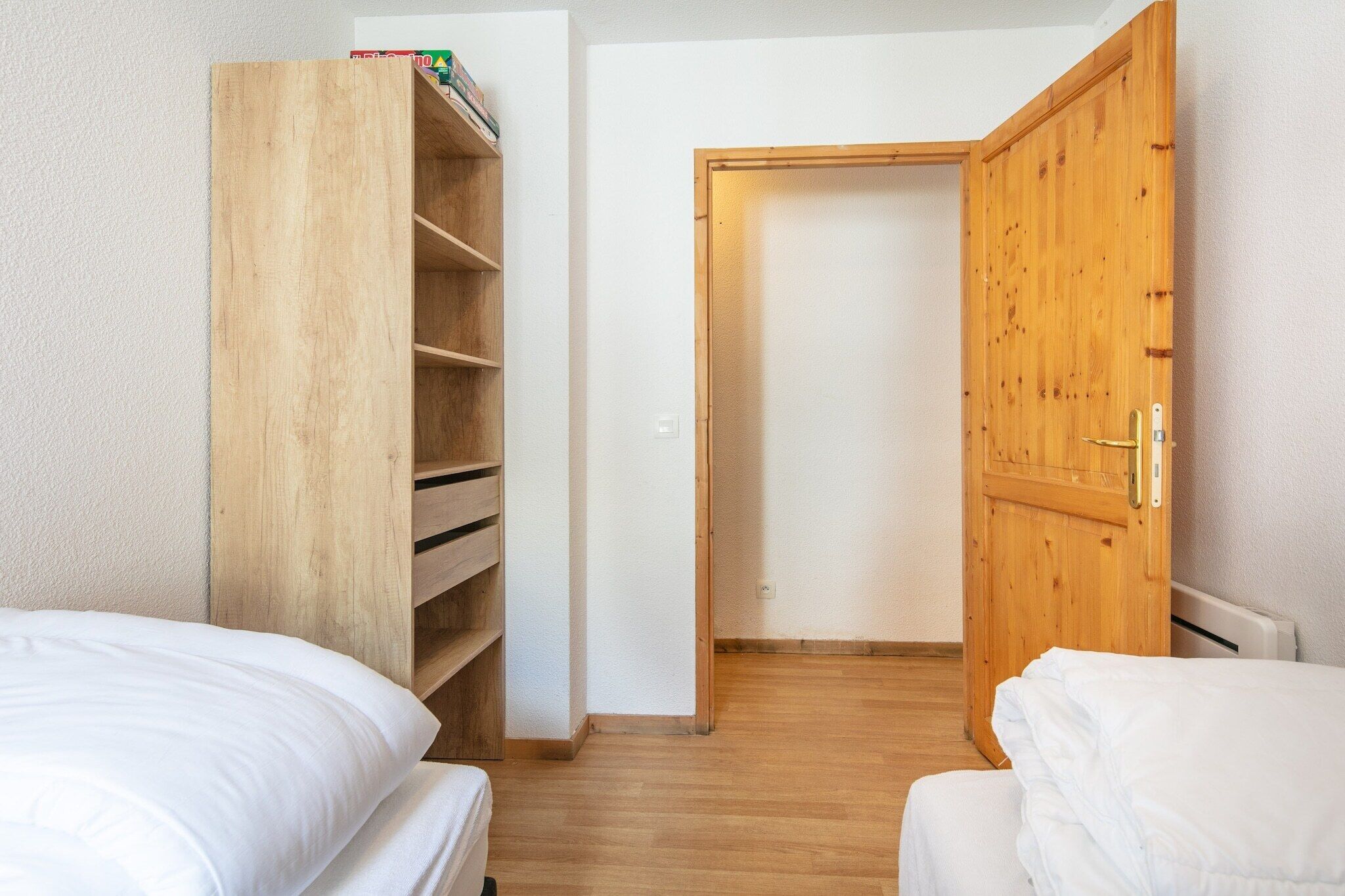 Une chambre avec deux lits, une armoire en bois et une porte donnant sur une autre pièce.