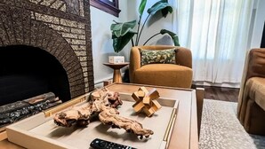 Ein Wohnzimmer mit Kamin, einer Couch, einem Couchtisch mit Dekoration und einer Pflanze.