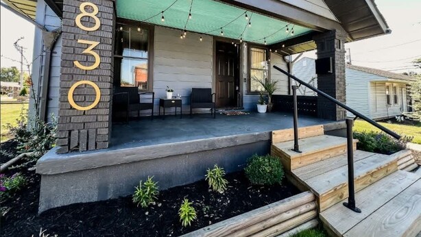 Ein modernes Haus mit überdachter Veranda, Hausnummer 830, und einer kleinen Sitzecke im Freien.