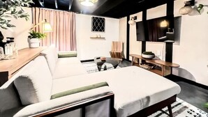 Ein modernes Schlafzimmer mit Schlafsofa, Fernseher, Schreibtisch und einem Blumentopf.