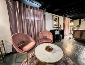 A modern living room with two pink chairs, a round table, and a large window with curtains.