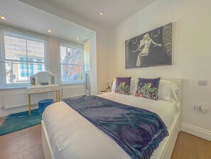 Een slaapkamer met een bed, een raam met zonwering, een radiator, een bureau en een schilderij aan de muur.