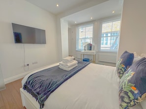 Relax in a serene bedroom with a made bed, flat-screen TV, and window with blinds.