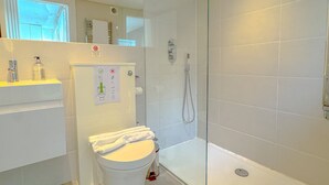 Un bany modern amb plat de dutxa envoltat de vidre, un vàter blanc i un lavabo amb mirall a la part superior.