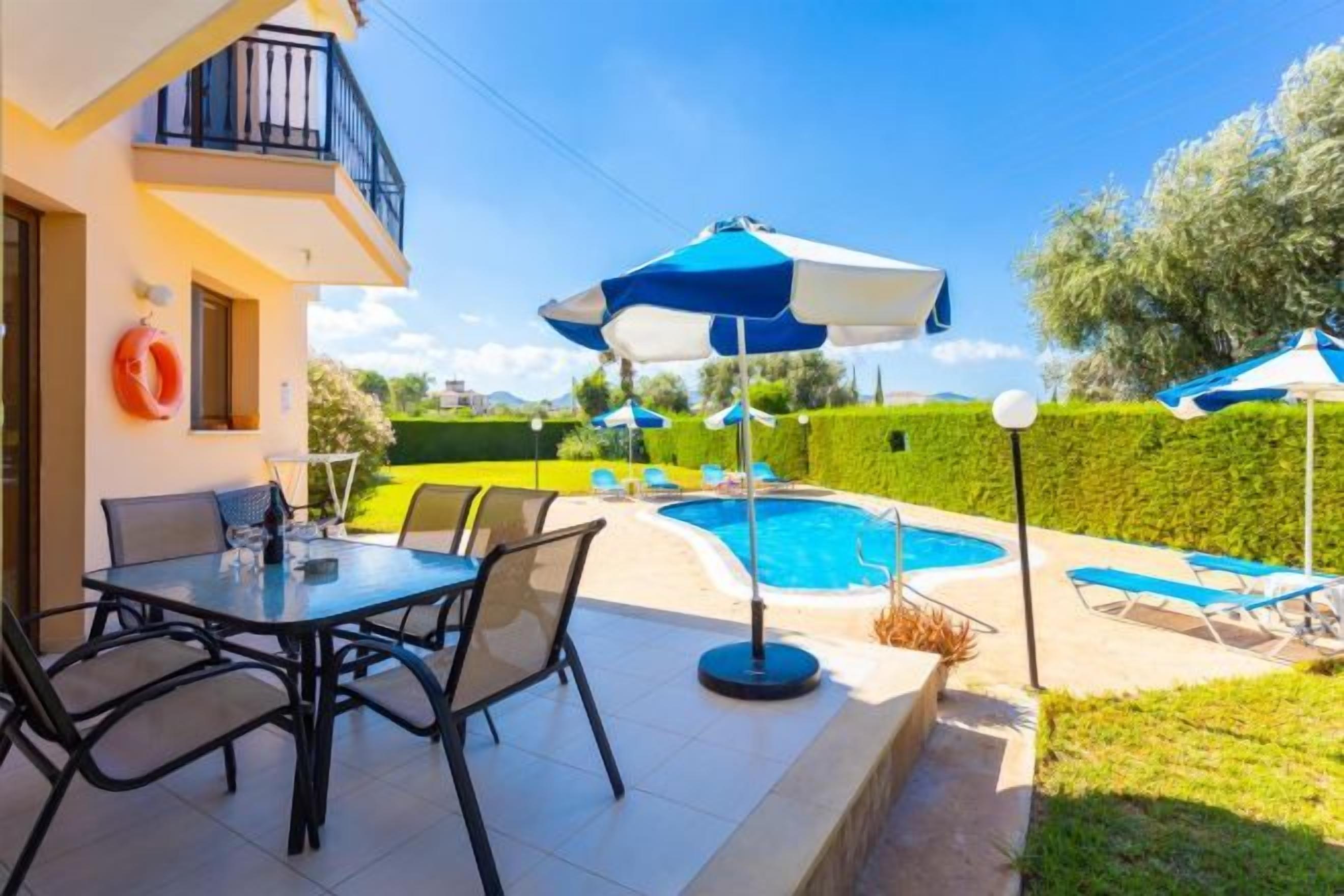 A poolside area with a table and chairs, a pool, and umbrellas.