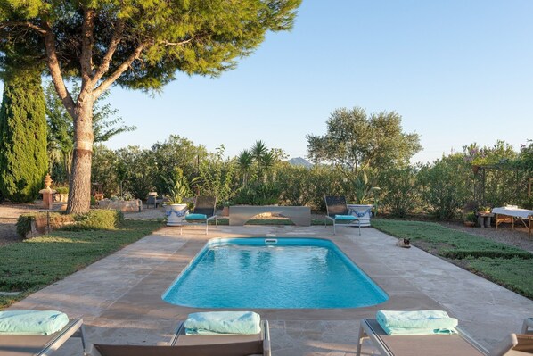 A rectangular pool with lounge chairs and a pergola in a landscaped backyard.