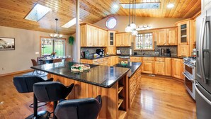 A spacious kitchen with wooden cabinets, a central island with bar stools, and a skylight. - Wild Timber Lodge: Golf Sim, Sauna, Bars, 10 acres, close to WI Dells (Oxford)