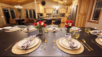 A dining table set with plates, cutlery, and wine glasses, surrounded by wooden cabinets and a chandelier.
