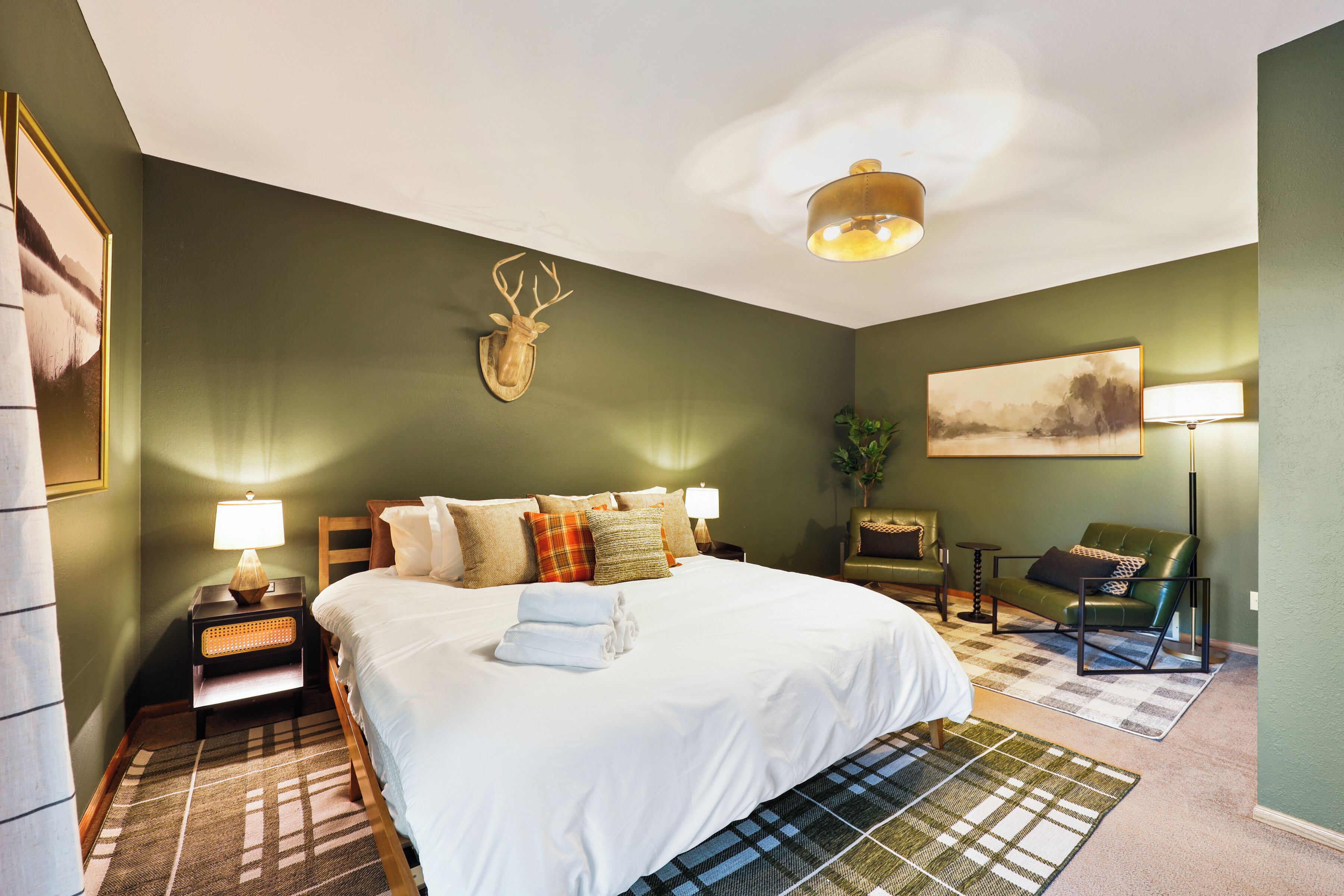 Une chambre d’hôtel avec un grand lit, une tête de cerf accrochée au mur, un canapé vert et une lampe.