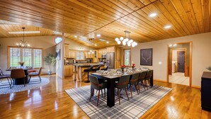 A spacious kitchen with wooden cabinets, a central island, and a dining area with a large table and chairs. - Wild Timber Lodge: Golf Sim, Sauna, Bars, 10 acres, close to WI Dells (Oxford)