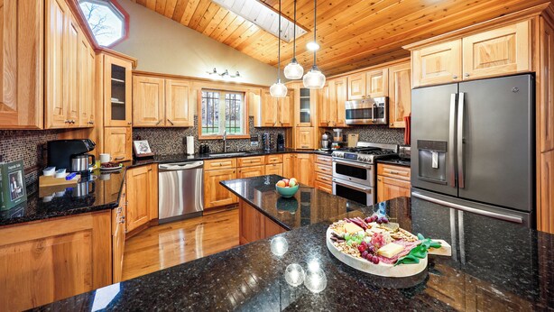 A spacious kitchen with wooden cabinets, a large island, stainless steel appliances, and pendant lighting. - Wild Timber Lodge: Golf Sim, Sauna, Bars, 10 acres, close to WI Dells (Oxford)