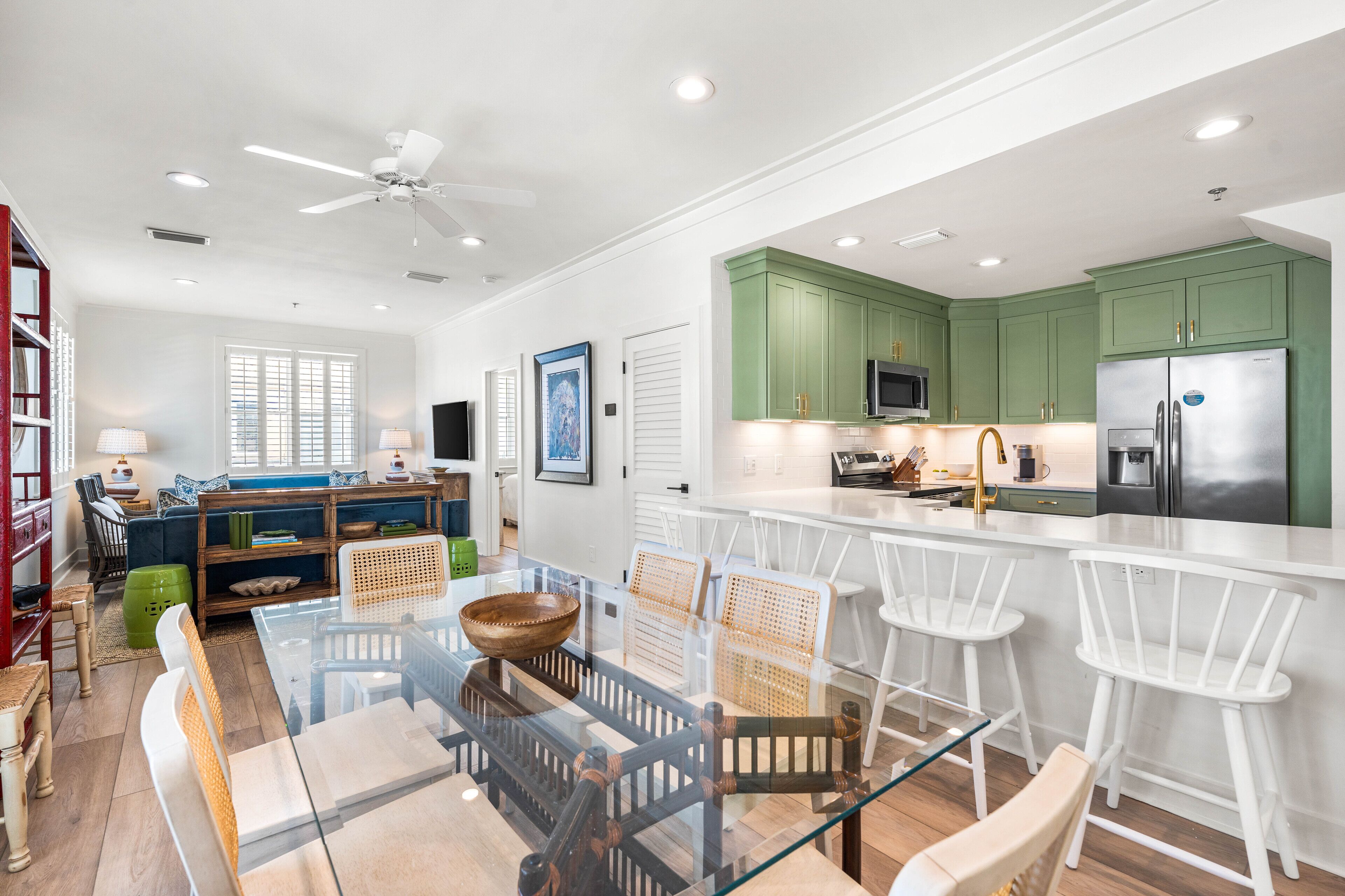 A modern kitchen with green cabinets, a stainless steel refrigerator, and a glass dining table with white chairs.