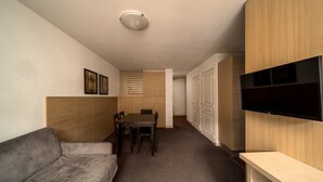 Un espace de vie compact comprenant un canapé, une table à manger avec des chaises, un téléviseur fixé au mur et des meubles de rangement en bois.