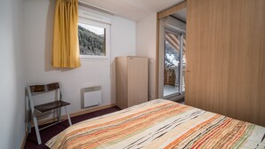 Une chambre à coucher comprenant un lit, une chaise, une fenêtre donnant sur un paysage enneigé, un radiateur et une armoire.