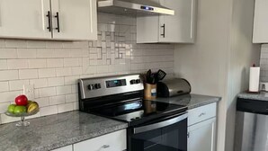 Une cuisine moderne avec des armoires blanches, une cuisinière en acier inoxydable et un dosseret carrelé.