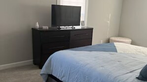 Une chambre à coucher avec un lit, une commode, un téléviseur et une fenêtre.