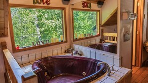 A bathroom with a large bathtub, two windows with 'LOVE' decorations, and a view of trees.