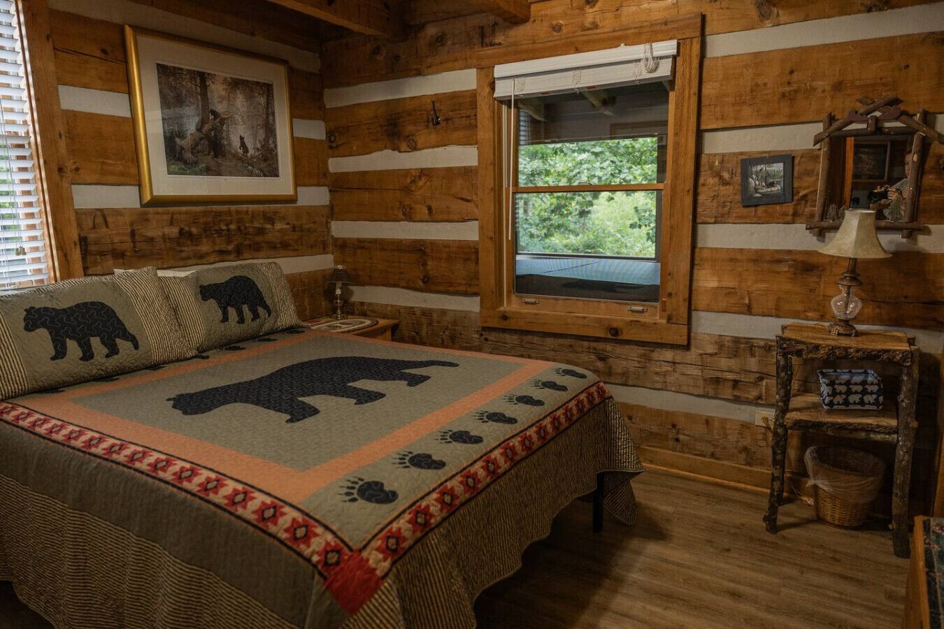 A log cabin bedroom with a bed featuring a bear-themed blanket, a window with a view of greenery, and a rustic wooden wall.