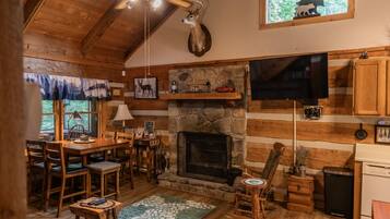 A cozy cabin interior with a stone fireplace, wooden furniture, a mounted deer head, and a television.