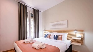 A neatly made bed with a white and orange bedspread, a wooden headboard, and a bedside table with a lamp.
