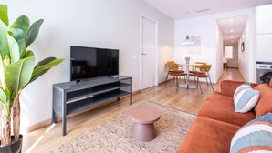 A modern living room with a flat-screen TV, a sofa, a dining area, and a kitchen in the background. - Sweett | Urgell Entresuelo I (Barcelona)