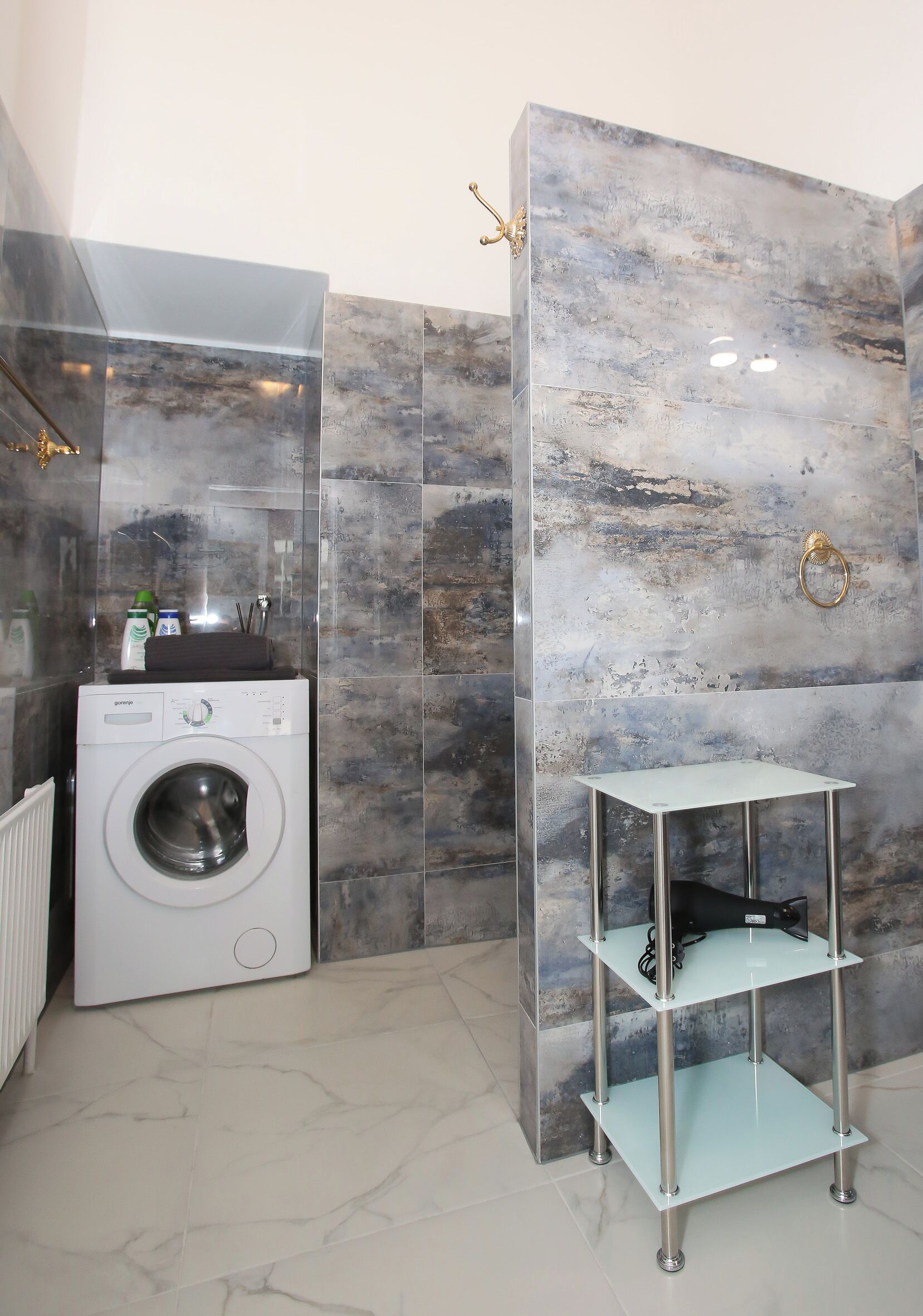 A modern bathroom with a washing machine, a glass shelf, and marble walls.