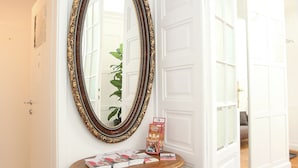 A room with a large ornate mirror on a wall, a small wooden table with magazines, and a door leading to another room.