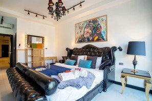 A bedroom with a large bed, a chandelier, a painting, and a side table. - Art Pool Villa (Pattaya)