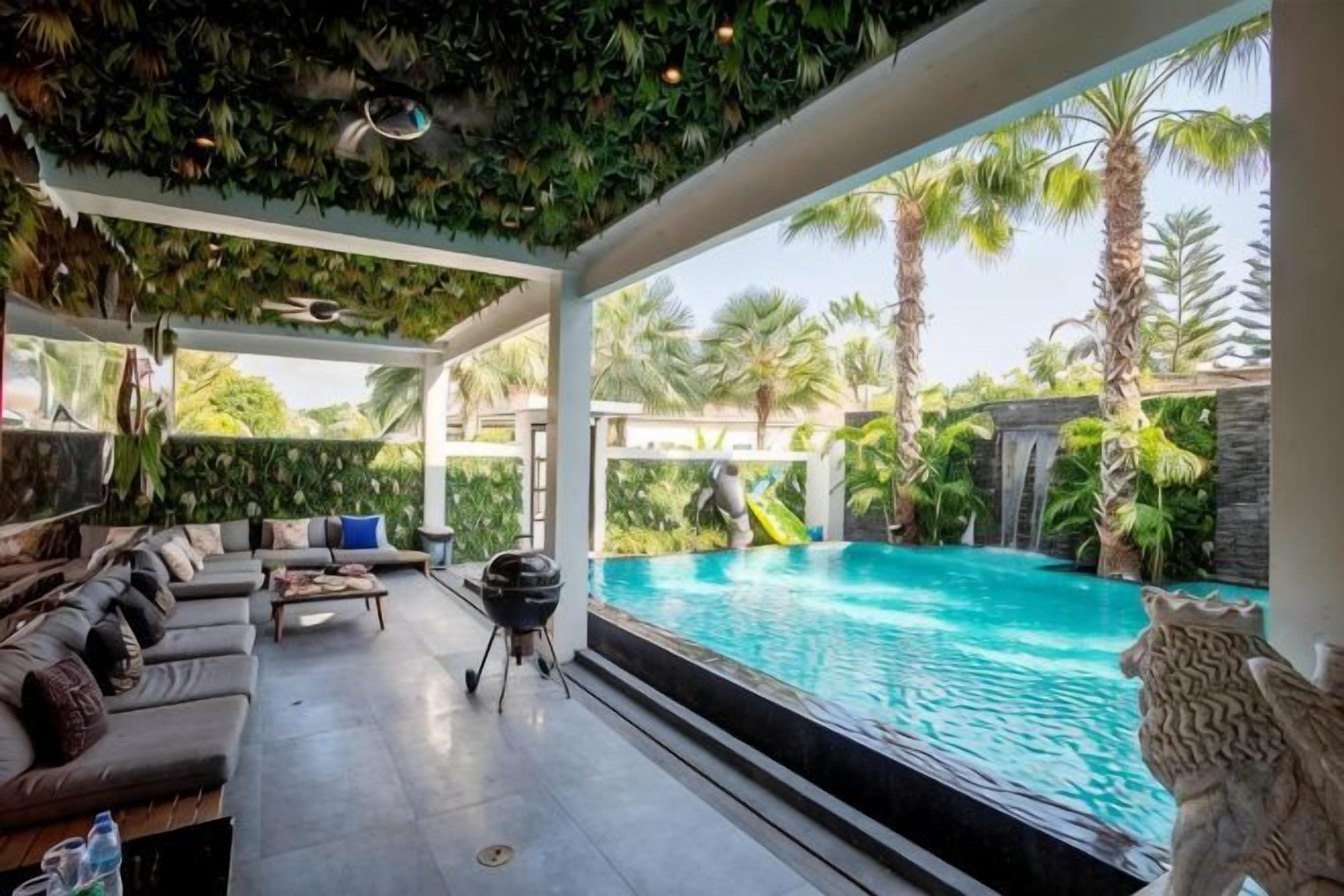 A poolside area with a lounge, a grill, and a view of a pool and palm trees.