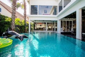 An indoor swimming pool with a dolphin sculpture, surrounded by palm trees and a modern building with large windows. - Art Pool Villa (Pattaya)