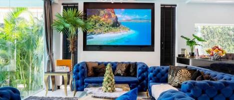 A modern living room with a large blue sofa, a coffee table, and a television mounted on the wall.