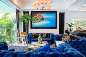 A modern living room with a large blue sofa, a coffee table, and a television mounted on the wall. - Art Pool Villa (Pattaya)