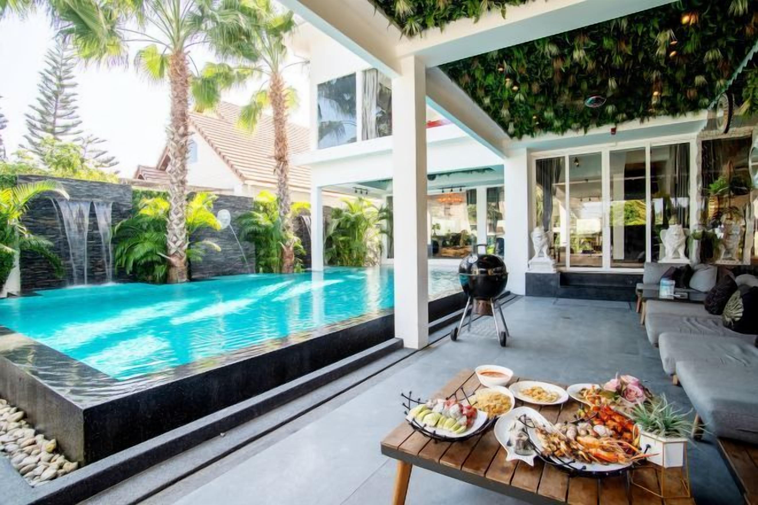 Un espace aménagé au bord de la piscine, avec une table à manger dressée pour un repas, un barbecue et un coin salon avec un canapé.