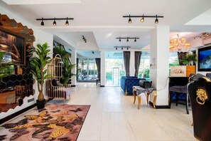 A spacious hotel lobby with a modern design, featuring a large seating area, a reception desk, and a television screen. - Art Pool Villa (Pattaya)