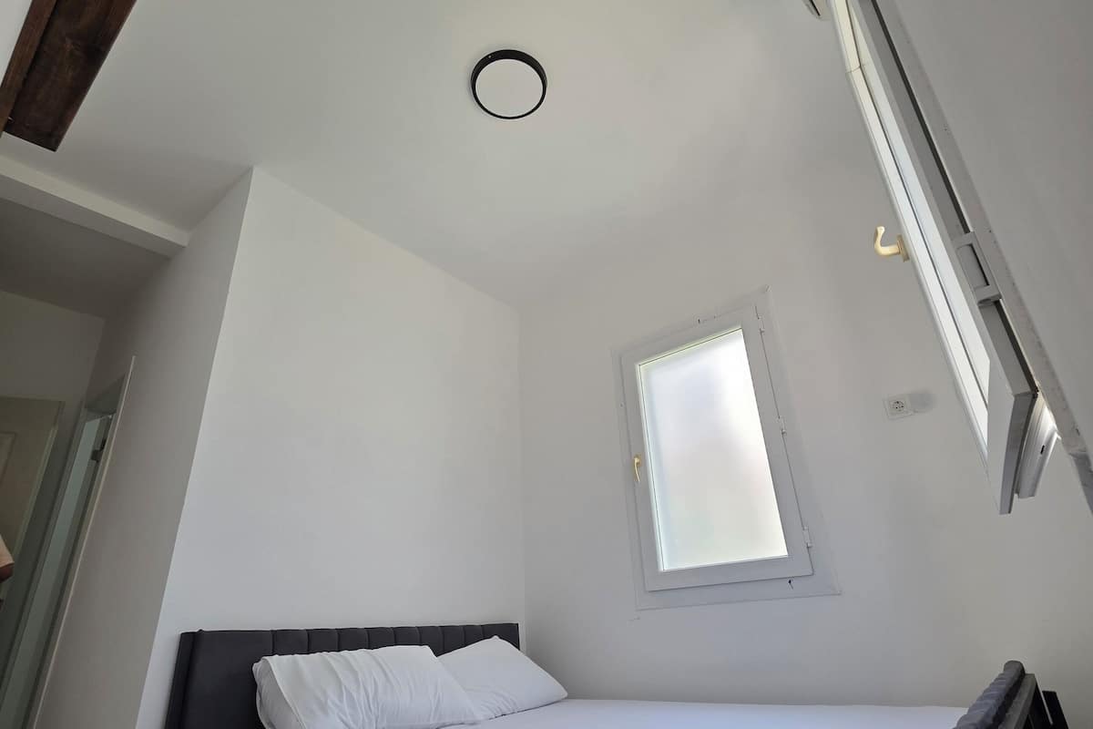 Ein kleines, helles Schlafzimmer mit einem Einzelbett, einem Fenster und einem Oberlicht.