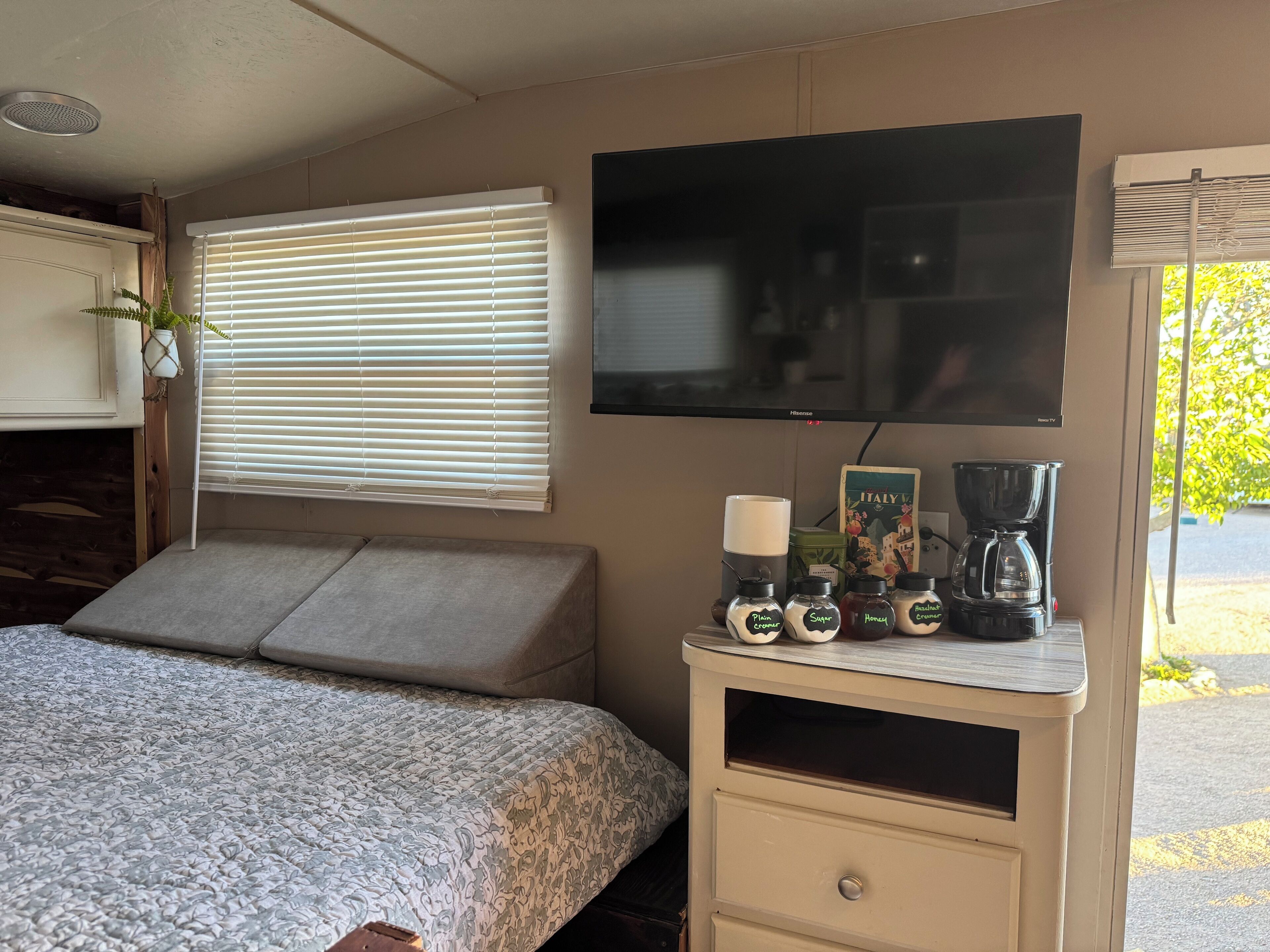 Een slaapkamer met een bed, een televisie, een koffiezetapparaat en een klein tafeltje met spullen erop.
