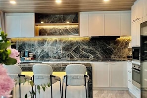 A modern kitchen with white cabinetry, a marble backsplash, and a built-in oven. - Mandla Villas Collection-Villa Tanya (Phuket)