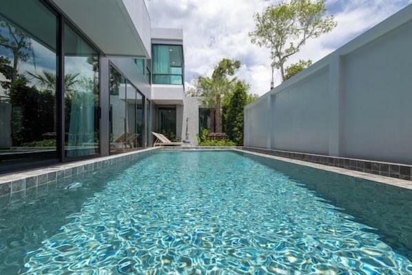 A modern pool area with clear water, surrounded by glass walls and a minimalist building. - Mandla Villas Collection-Villa Tanya (Phuket)